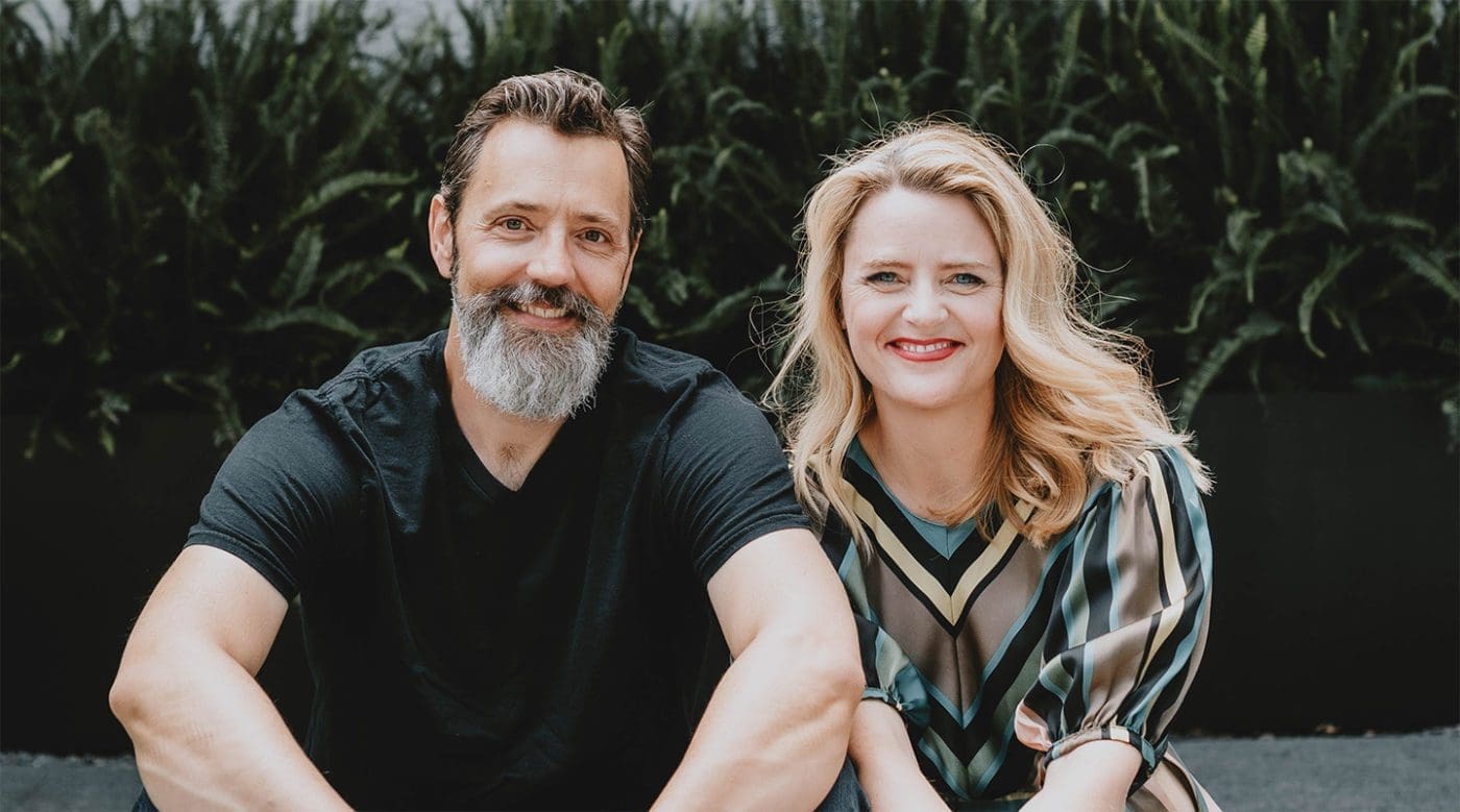 Craig and Sara Jenkins-Sutton sitting side by side with a greenery background.