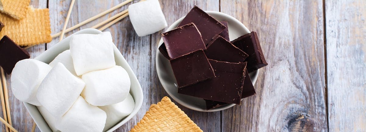 Close up of s'mores fixings in bowls on a wooden table.
