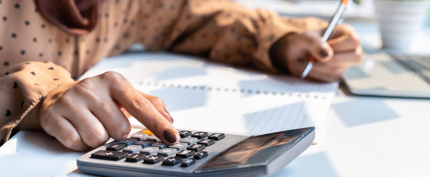 Hands typing on a calculator and writing in a notebook with the other hand.