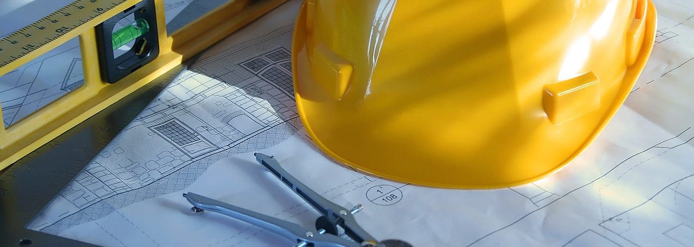 Yellow hard hat on top of drawn landscaping plans and a level.