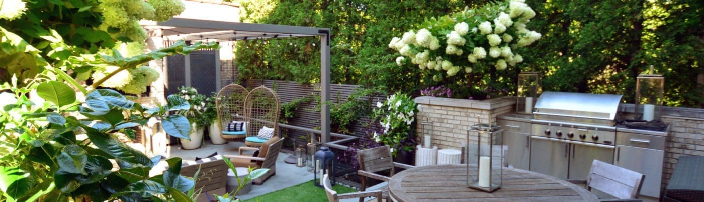 Outdoor kitchen with a grill, round table for dining, and a sitting area in an abundance of greenery.