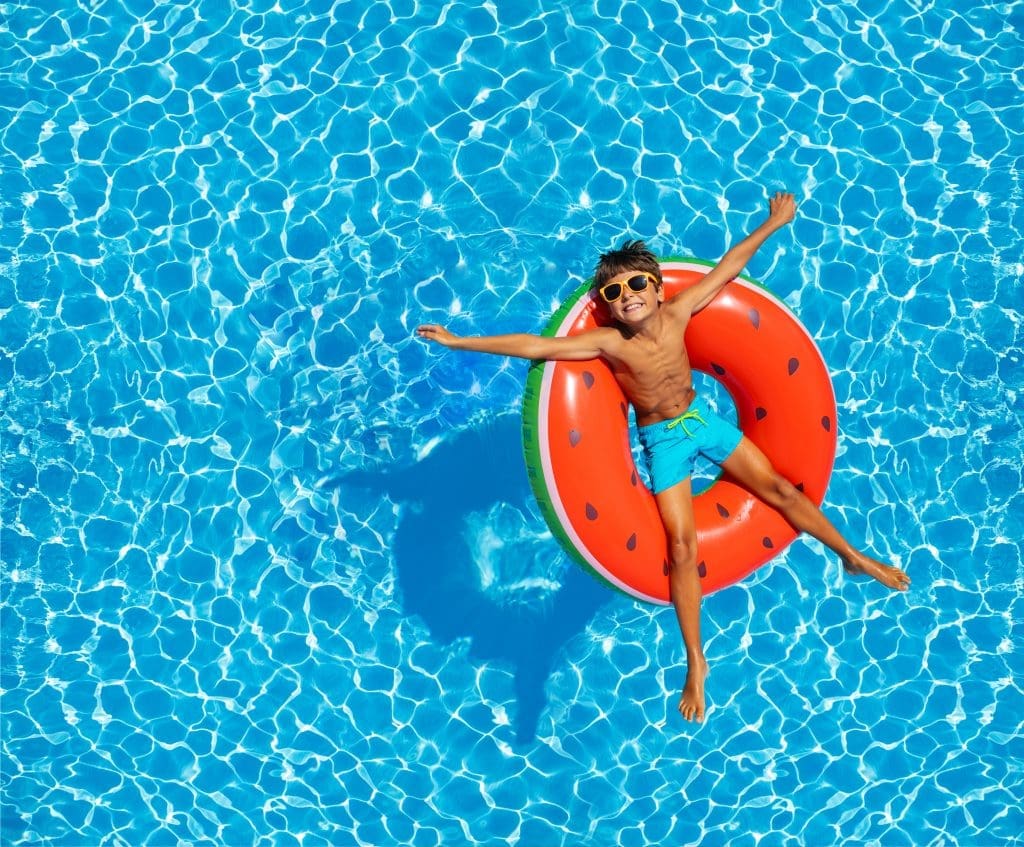 Little boy swim on inflatable melon color ring with happy expression view from above